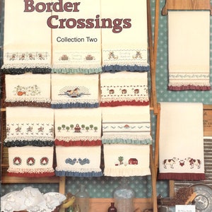 May include: A book titled "Border Crossings Collection Two" featuring cross-stitch patterns for towels. The book cover shows a variety of towels with different cross-stitch designs, including a country store, a farmhouse, and a barn.