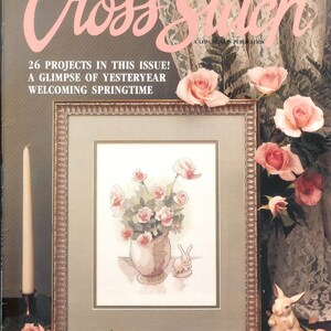 May include: A magazine cover for Cross Stitch magazine, featuring a cross stitch design of a vase of pink roses and a bunny rabbit. The cover text reads "For the Love of Cross Stitch" and "26 Projects in this Issue! A Glimpse of Yesteryear Welcoming Springtime".