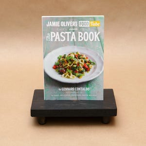 Pode incluir: Um livro de receitas intitulado "The Pasta Book" de Gennaro Contaldo, apresentado pelo Jamie Oliver's Food Tube. A capa apresenta uma foto de um prato de massa com tomates, manjeric&atilde;o e outros vegetais.
