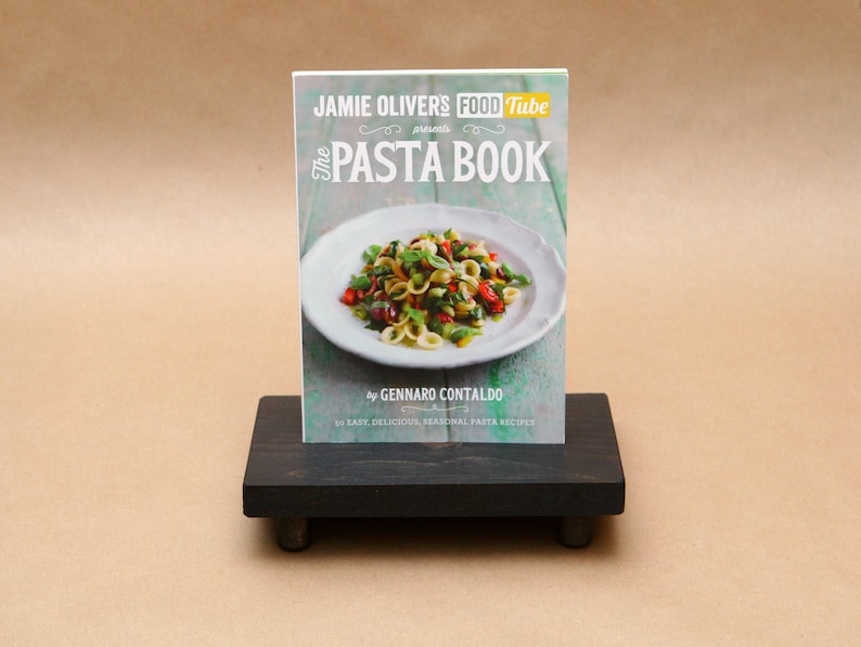 Pode incluir: Um livro de receitas intitulado "The Pasta Book" de Gennaro Contaldo, apresentado pelo Jamie Oliver's Food Tube. A capa apresenta uma foto de um prato de massa com tomates, manjeric&atilde;o e outros vegetais.