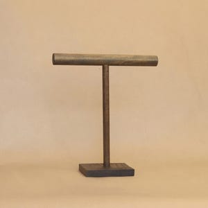 May include: A dark brown wooden T-shaped jewelry display stand featuring a horizontal cylindrical bar supported by a vertical post attached to a square base. The stand has a smooth, matte finish and is constructed from solid wood components.