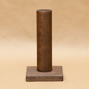 May include: A dark brown wooden stand with a cylindrical top and a square base. The stand is made of wood and has a natural finish.