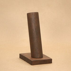 May include: A dark brown wooden stand with a cylindrical top for displaying bracelets or watches.