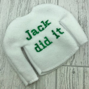 May include: White elf-sized sweater with long sleeves and green embroidered text that reads "Jack did it".