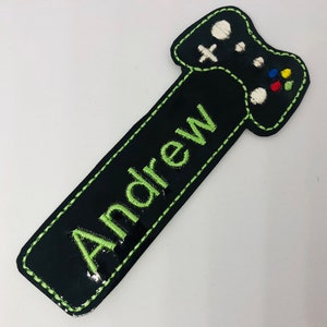 May include: Black and green fabric bookmark with a green embroidered video game controller and the name "Andrew" in green embroidery.