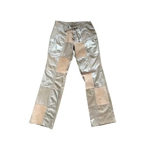 May include: Beige pants with a patchwork design featuring a combination of smooth and textured fabric. The pants have a lace-up detail at the front.