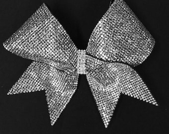 May include: A large silver sparkly bow with a pointed center. The bow is made of many small, shiny rhinestones.
