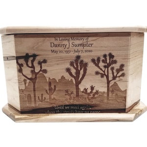 May include: A wooden urn with a desert landscape design. The light-colored wood urn features engraved Joshua trees, cacti, and mountains. Text reads "In Loving Memory of Danny J Sumpter, May 20, 1951 - July 7, 2020" and "Until we meet again, where the streets have no name."