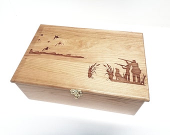 Könnte beinhalten: Eine Holzkiste mit einem Scharnierdeckel und einem Messingverschluss. Der Deckel ist mit einem eingebrannten Design von drei Jägern mit einem Hund in einem Sumpf verziert, über dem Enten fliegen.