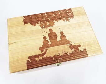 Könnte beinhalten: Eine Holzkiste mit einem Laser-gravierten Design von drei Figuren, die unter einem Baum angeln. Die Kiste hat einen Messingverschluss und das Wort "Papa" ist auf der Vorderseite graviert.