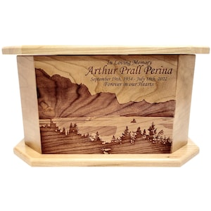 May include: A wooden cremation urn with a laser engraved image of a mountain lake scene. The urn is inscribed with "In Loving Memory Arthur Prall Perina September 19th, 1954 - July 18th, 2022 Forever in our Hearts."
