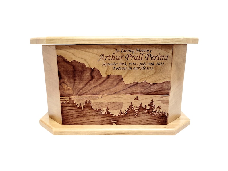 May include: A wooden cremation urn with a laser engraved image of a mountain lake scene. The urn is inscribed with "In Loving Memory Arthur Prall Perina September 19th, 1954 - July 18th, 2022 Forever in our Hearts."
