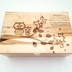 Peut inclure: Coffret souvenir en bois clair avec un motif de grain de bois. Le couvercle présente un motif gravé de deux hiboux sur une branche, avec le texte "Shivam, I'll love you forever...My baby you'll be". Le coffret a un petit fermoir en métal.