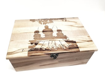 May include: A wooden box with a hinged lid and a metal latch. The lid is decorated with a laser-engraved design of three figures sitting on a bench under a tree.