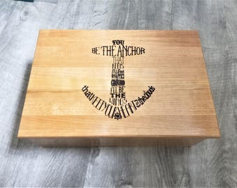 Puede incluir: Una caja rectangular de madera clara. La parte superior presenta un diseño de ancla negro con las palabras: "You be the anchor that keeps my feet on the ground, I'll be the wings that keep your heart in the clouds."