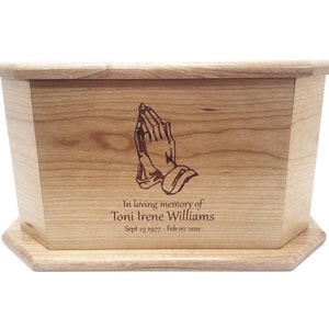 May include: A wooden cremation urn with a praying hands design and the inscription "In loving memory of Toni Irene Williams Sept 23 1977 - Feb 07 2021"
