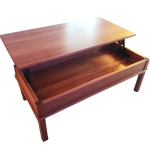 May include: A wooden coffee table with a lift-top mechanism. The top is raised to reveal a storage compartment.