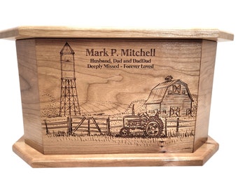 May include: A wooden urn with a light brown finish. The urn features an engraved farm scene with a water tower, barn, tractor, and the text "Mark P. Mitchell, Husband, Dad and DadDad, Deeply Missed - Forever Loved."