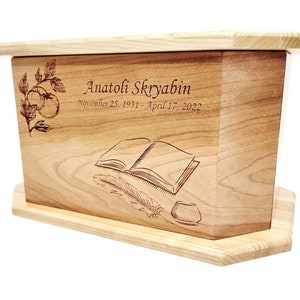 May include: A wooden cremation urn with a personalised inscription for Anatoli Skryabin, November 25, 1931 - April 17, 2022. The urn features an engraved design of a book, a quill pen, and an inkwell.