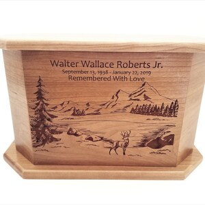 May include: A wooden cremation urn with a laser-engraved scene of a lake, mountains, trees, and a deer. The urn is inscribed with "Walter Wallace Roberts Jr. September 13, 1938 - January 22, 2019 Remembered With Love."