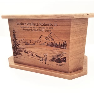 May include: A wooden cremation urn with a laser engraved image of a mountain scene with a deer in the foreground. The urn is inscribed with the name "Walter Wallace Roberts Jr." and the dates "September 13, 1938 - January 22, 2019". The inscription also includes the phrase "Remembered With Love".