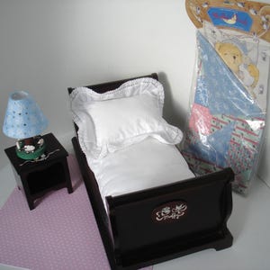May include: A miniature bedroom set featuring a dark brown bed with a white pillow and bedding, a matching nightstand with a blue lamp, and a packaged quilt. The lamp has a blue shade with white stars.