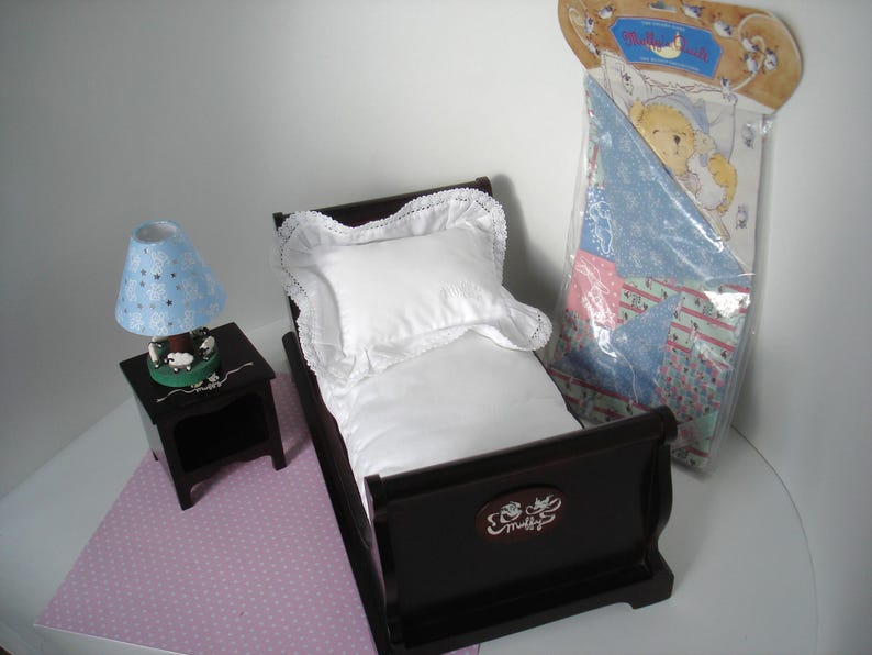 May include: A miniature bedroom set featuring a dark brown bed with a white pillow and bedding, a matching nightstand with a blue lamp, and a packaged quilt. The lamp has a blue shade with white stars.
