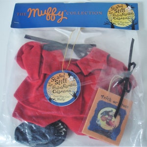May include: A red devil costume set in a clear plastic bag. The set includes a red outfit, black horns, and a small orange bag with the words "Trick or Treat". The packaging includes the text "The Muffy Collection".