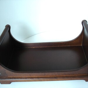 May include: A dark brown wooden tray with a curved design. The tray has a rectangular base and curved sides with rounded ends. The wood has a smooth finish and appears to be stained. The tray is likely for decorative or organizational purposes.
