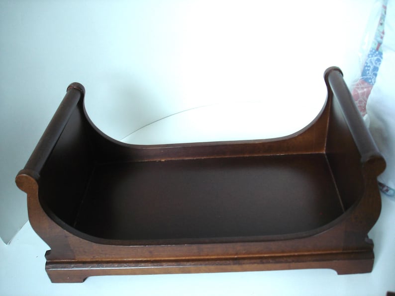 May include: A dark brown wooden tray with a curved design. The tray has a rectangular base and curved sides with rounded ends. The wood has a smooth finish and appears to be stained. The tray is likely for decorative or organizational purposes.
