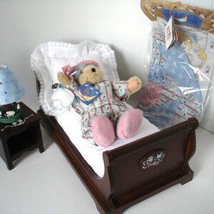 May include: A miniature bedroom set featuring a teddy bear in pajamas lying in a wooden bed with a white pillow and blanket. A blue lamp with star cutouts sits on a nightstand. A packaged quilt is also present.