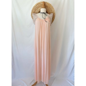 May include: A pale pink nightgown on a mannequin. The gown has a flowing, floor-length design with delicate lace sleeves. A straw hat rests on the mannequin's head, and a black ribbon is tied around the neck.
