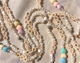 May include: Three layered necklaces with white pearl beads and colorful heart-shaped beads. The necklaces are made with different bead patterns and include small, speckled beads.