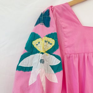 K&ouml;nnte beinhalten: Rosa Baumwollkleid mit gestickten Schmetterlingen und Blumen an den &Auml;rmeln. Das Kleid hat einen quadratischen Ausschnitt und einen gerafften Rock.