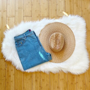 May include: A light blue pair of jeans and a woven straw hat on a white fluffy rug.