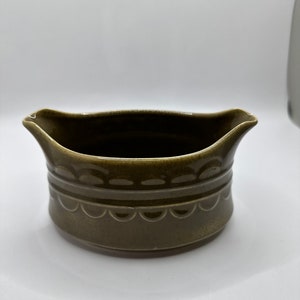 May include: A green ceramic gravy boat with a scalloped edge and a decorative pattern around the middle.