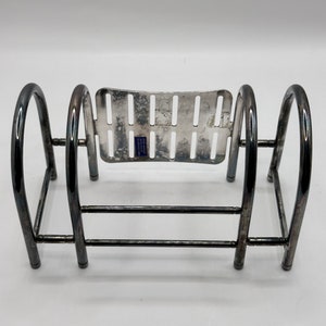 May include: Silver-plated metal utensil holder with a rectangular base and two curved sides. The holder has a wire rack with a grid pattern on the top and a second wire rack below.