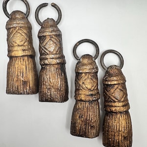May include: Four decorative tassels with a metallic gold finish and dark metal rings. The tassels have a textured, carved design and are arranged on a white background. The tassels vary slightly in size.