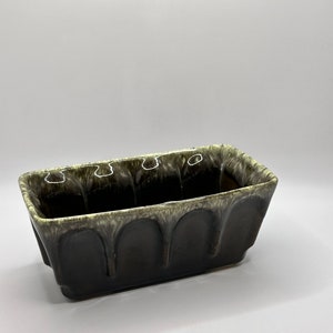 May include: A rectangular ceramic planter with a dark green glaze and a light green swirl pattern. The planter has a slightly rounded bottom and a rectangular opening.