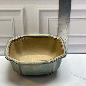 May include: A rectangular ceramic planter with rounded corners, featuring a green and brown glazed finish. A metal ruler is placed vertically next to the planter, showing the height is approximately 3 inches tall.
