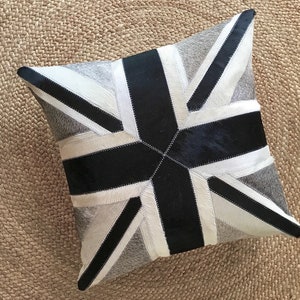 May include: Square cushion with a Union Jack design. The cushion is made from a patchwork of grey, black, and white leather. The design is a stylized representation of the British flag.
