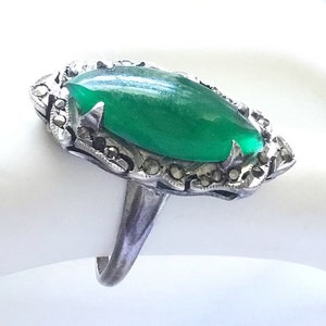 May include: A silver ring with a large green stone set in a marcasite design.