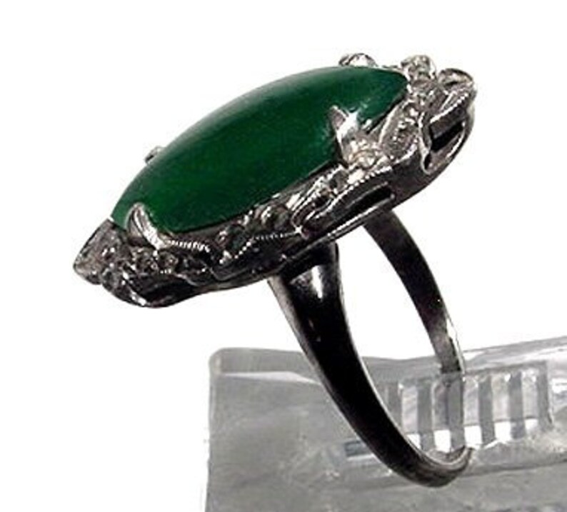 May include: A vintage ring with a large, oval-shaped green jade stone set in a delicate silver filigree design.
