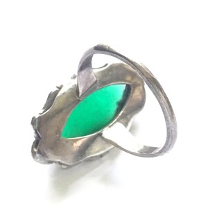 May include: A silver ring with a green gemstone set in a detailed filigree design.
