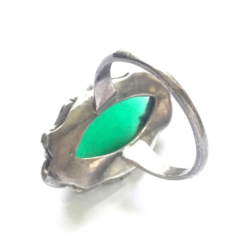 May include: A silver ring with a green gemstone set in a detailed filigree design.