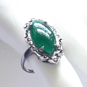 May include: A silver ring with a green oval gemstone surrounded by a detailed silver setting with small stones.