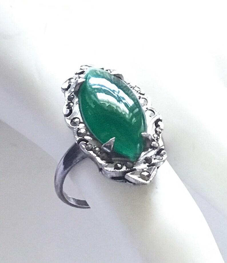 May include: A silver ring with a green oval gemstone surrounded by a detailed silver setting with small stones.