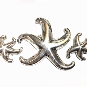 May include: Three silver starfish of varying sizes, arranged in a row. The largest starfish is in the center, with the two smaller starfish on either side.