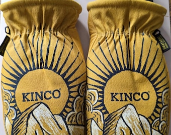 May include: A pair of yellow leather mittens with a black and white mountain and sun design. The word "KINCO" is printed on each mitten. The cuffs are black and ribbed. The text "AMT Designs" is in the upper right corner.