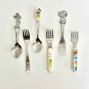 May include: A collection of children's silverware, including spoons and forks. The spoons feature Mickey Mouse and Snoopy designs. The forks have character-themed handles, with one featuring a colorful design. The silverware is made of stainless steel.